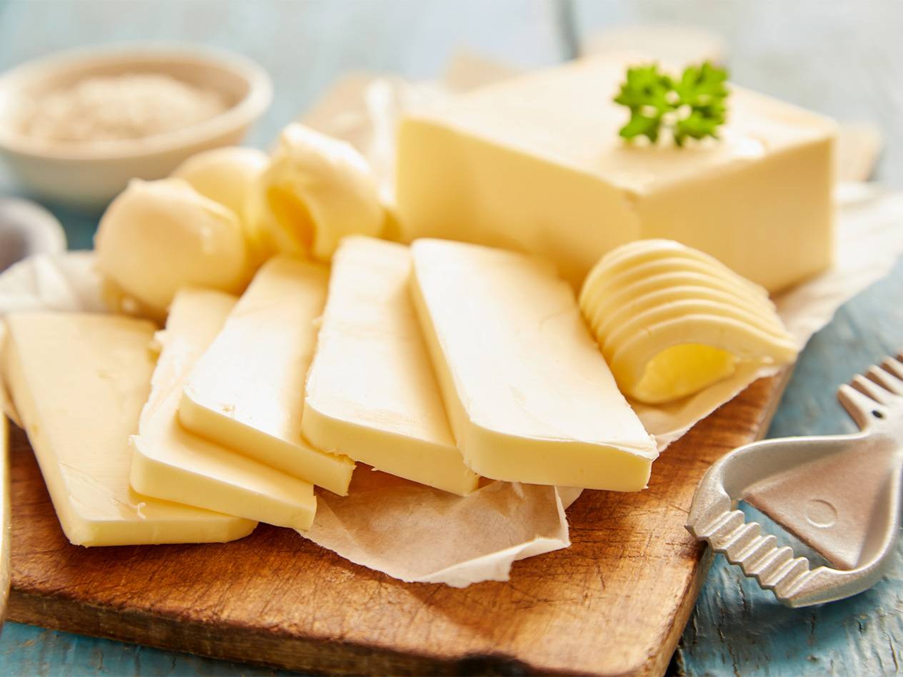Frische Butterstücke und -rollen auf einem Holzbrett, bereit zum Verarbeiten.