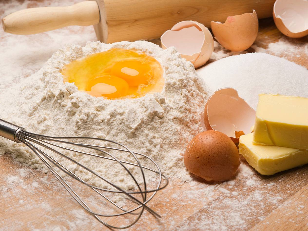 Zutaten für Gebäck: Mehl, Eier, Zucker, Butter und Schneebesen.