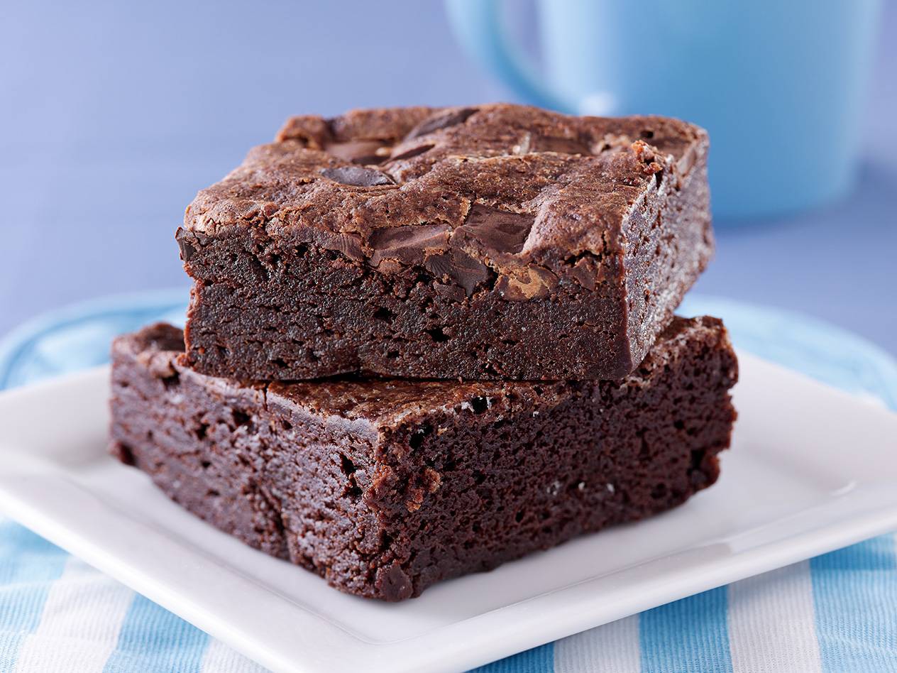 Zwei schokoladige Brownies liegen übereinander auf einem weißen Teller.
