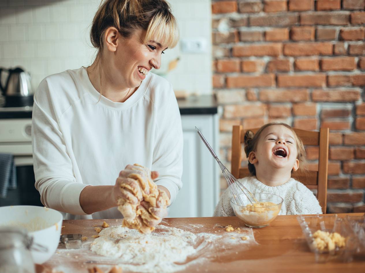 Eine Mutter und ihre Tochter backen zusammen fröhlich Kekse in der Küche.