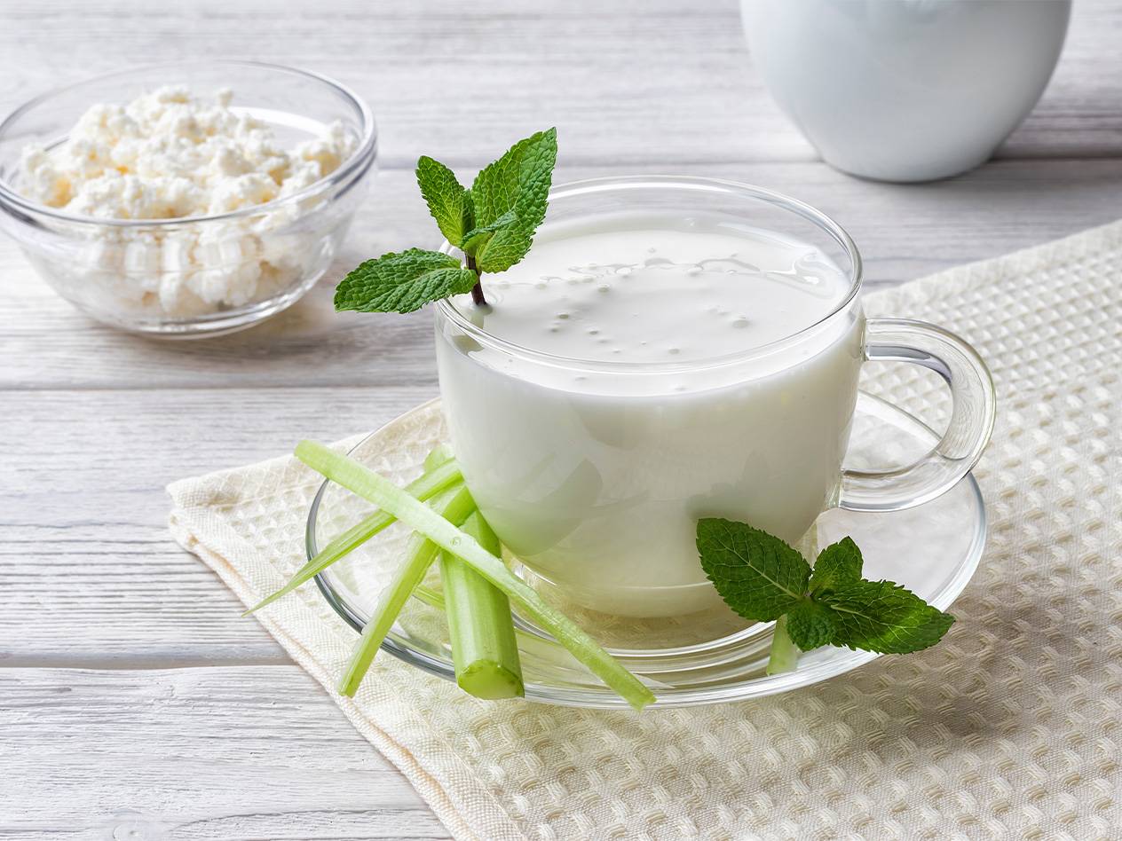 Ein Glas Kefir mit Minze und Sellerie auf einem Tisch neben einer Schüssel mit Quark.