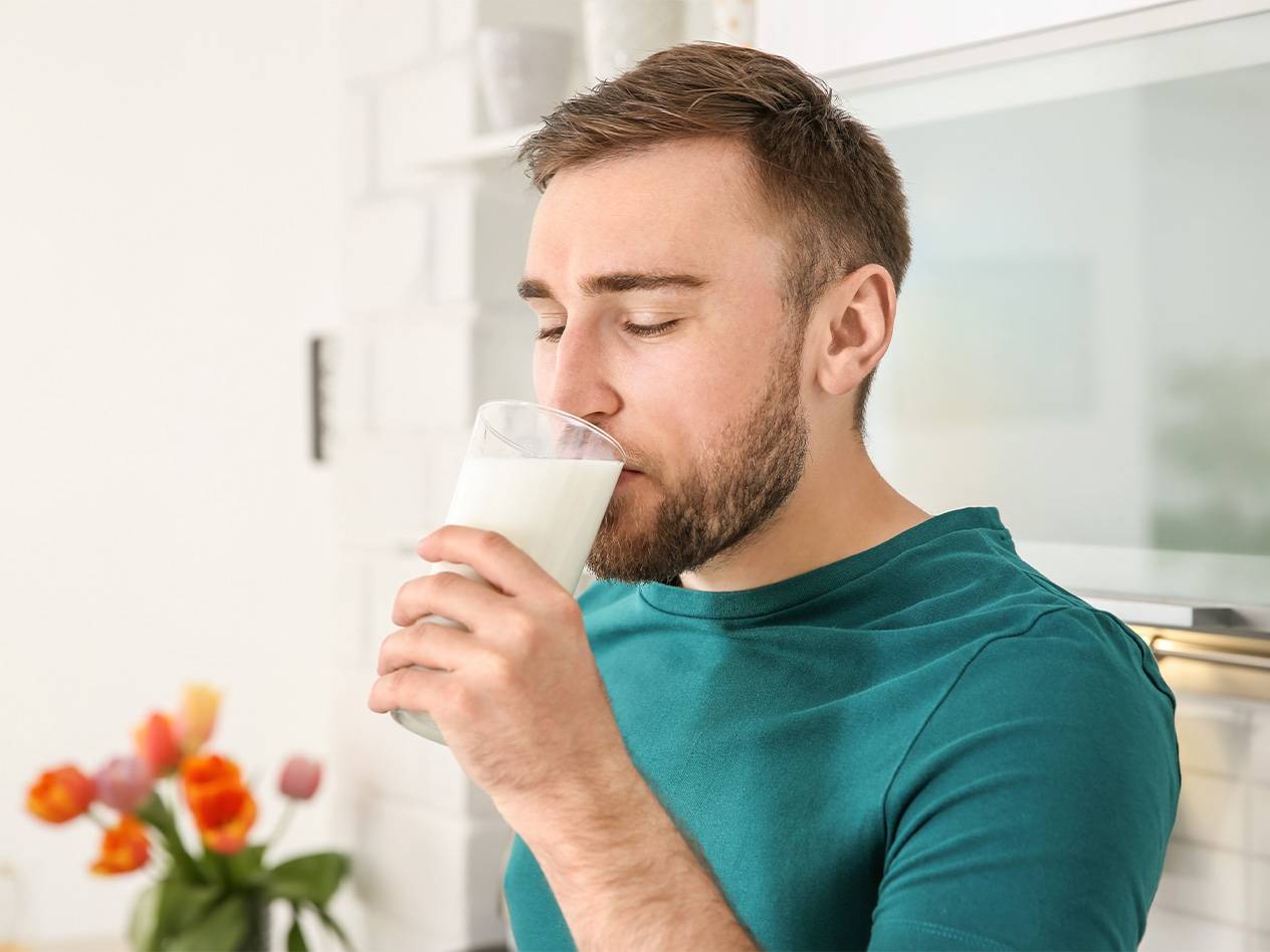 Ein Mann trinkt ein Glas Milch in seiner Küche.