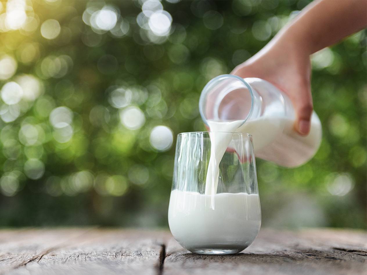 Eine Hand gießt Milch aus einer Karaffe in ein Glas.