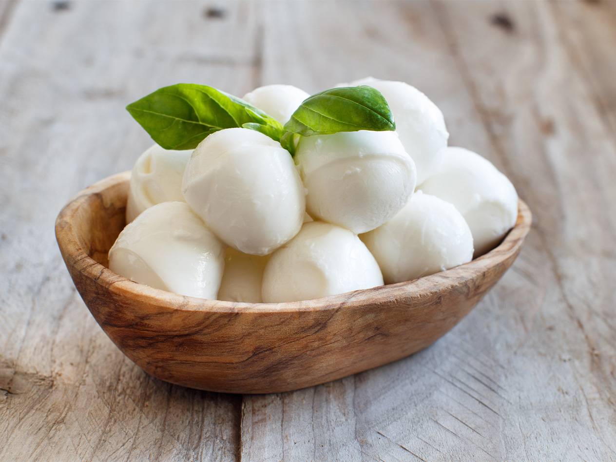 Kleine Mozzarellakugeln in einer Holzschale mit Basilikum.