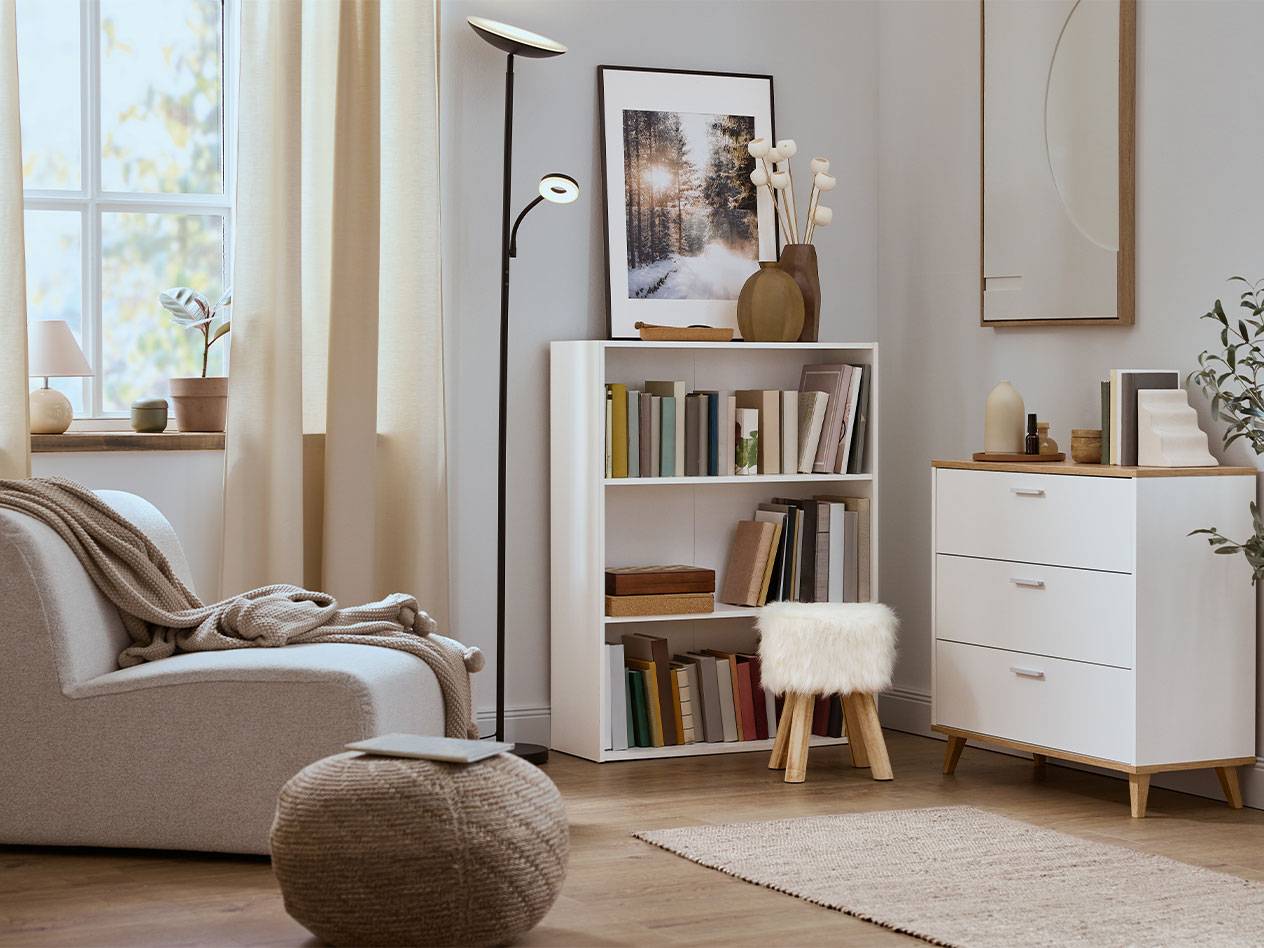 Gemütliches Wohnzimmer mit Sessel, Bücherregal und Kommode in neutralen Farben.