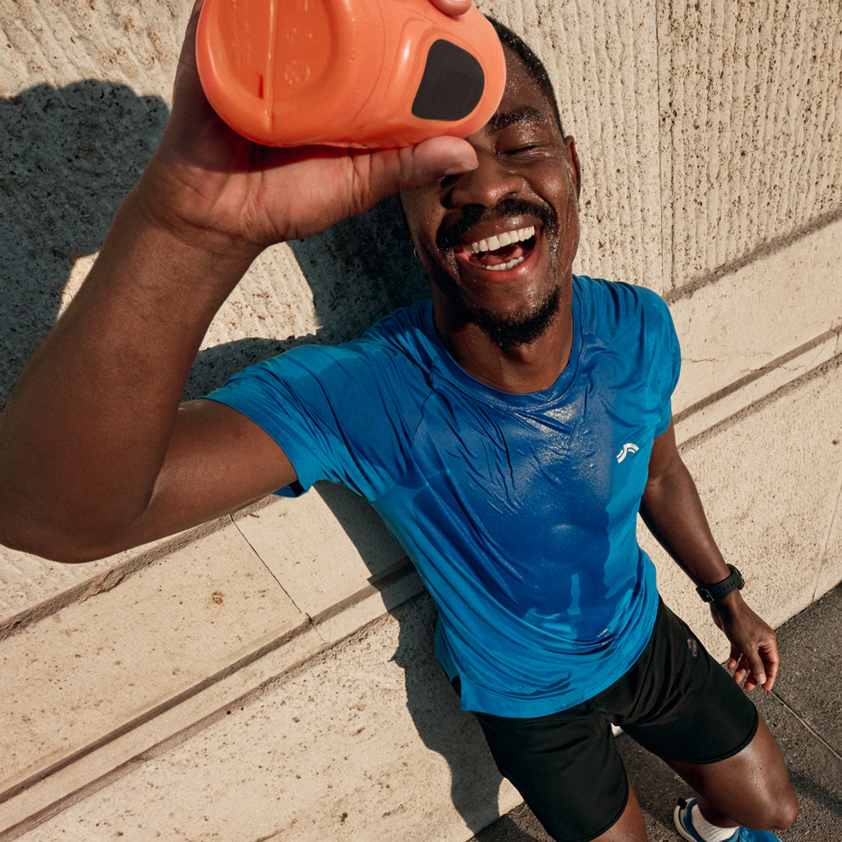 Mann in blauem Sport-T-Shirt und schwarzen Shorts gießt sich nach dem Training Wasser über.