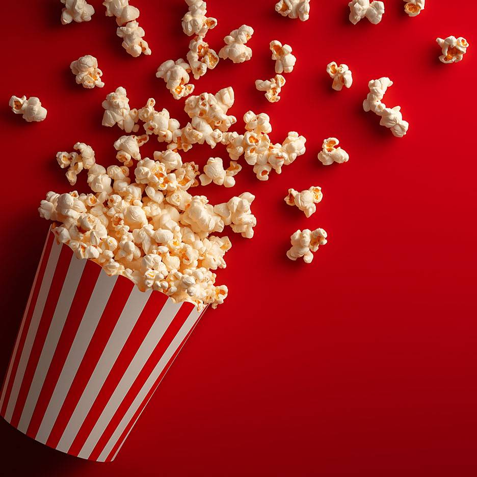 Popcorn auf rotem Hintergrund, ein Teil des Popcorns in einem gestreiften Pappbecher.