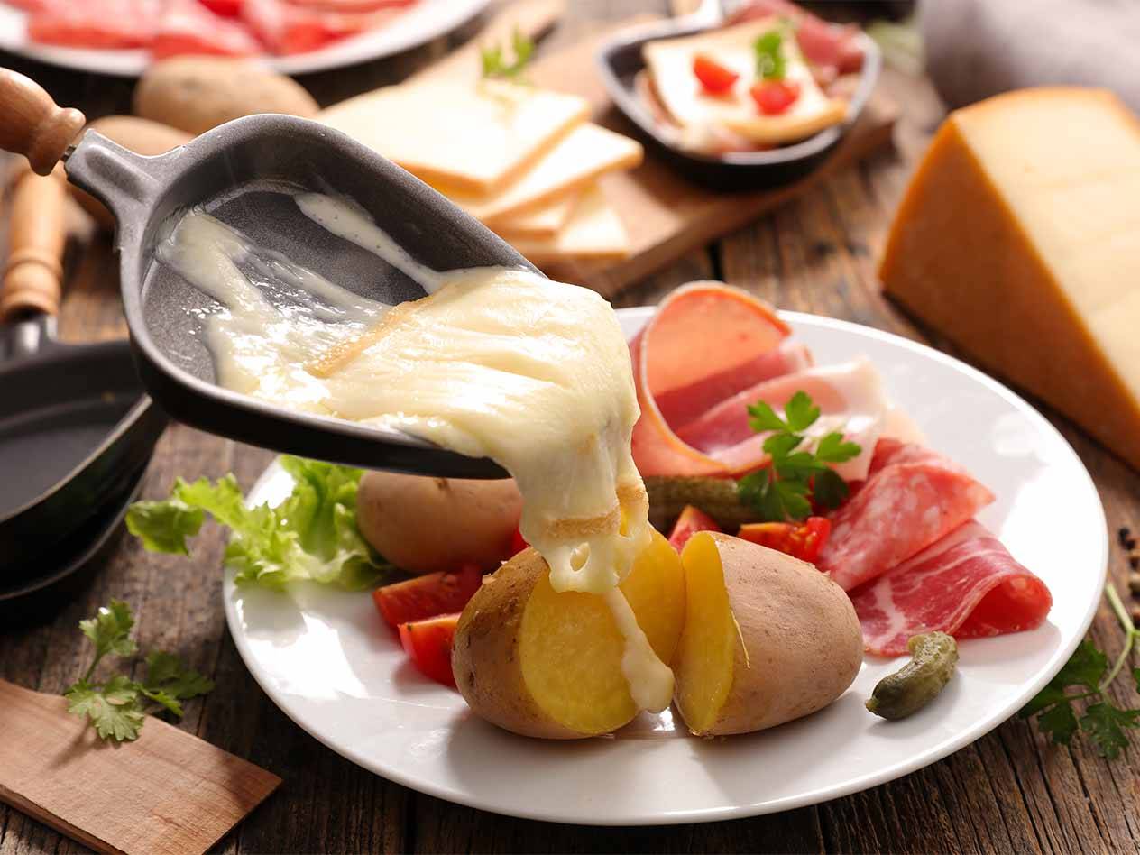 Geschmolzener Raclette-Käse wird über Kartoffeln und Wurstwaren gegossen.