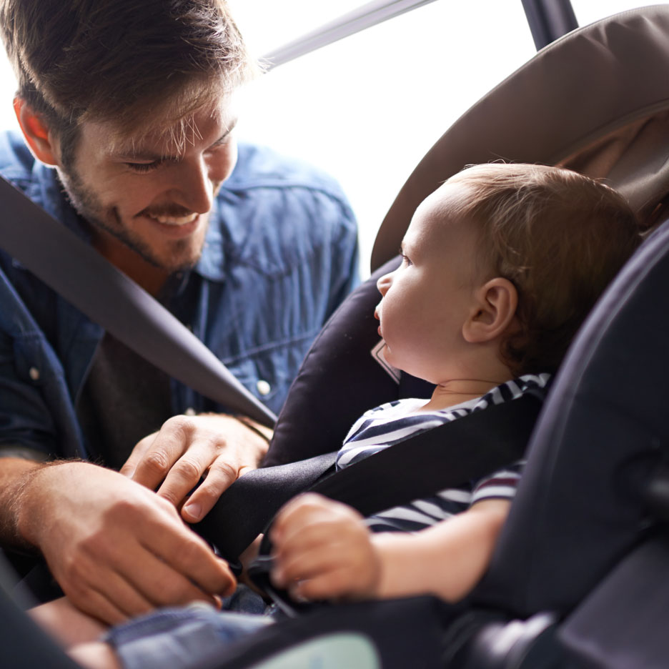 Ein Vater schnallt sein Baby in einen Autositz.