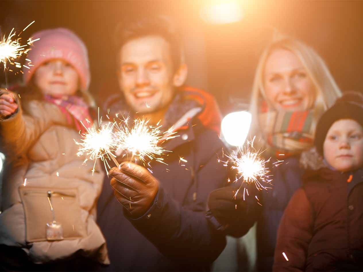 Eine Familie mit zwei Kindern hält Wunderkerzen in der Dunkelheit.