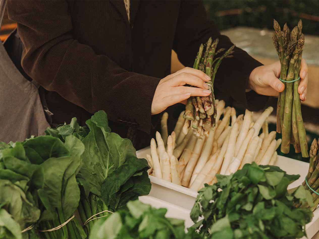 Eine Person hält Bündel von grünem und weißem Spargel auf einem Markt.