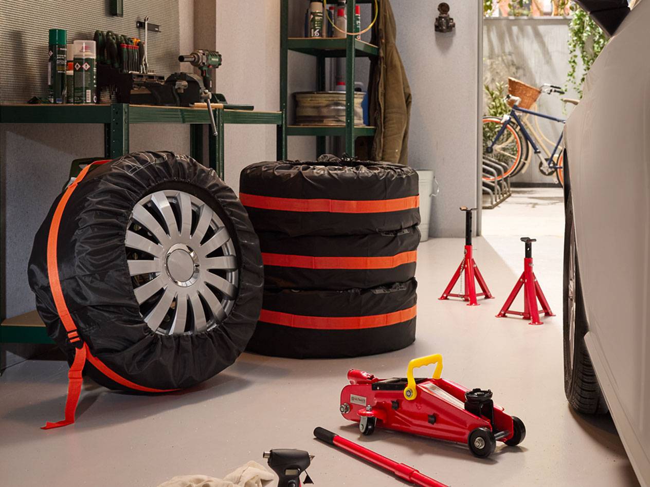 Winterreifen verpackt mit Hüllen, hydraulische Wagenheber und Auto-Ständer in einer Garage.