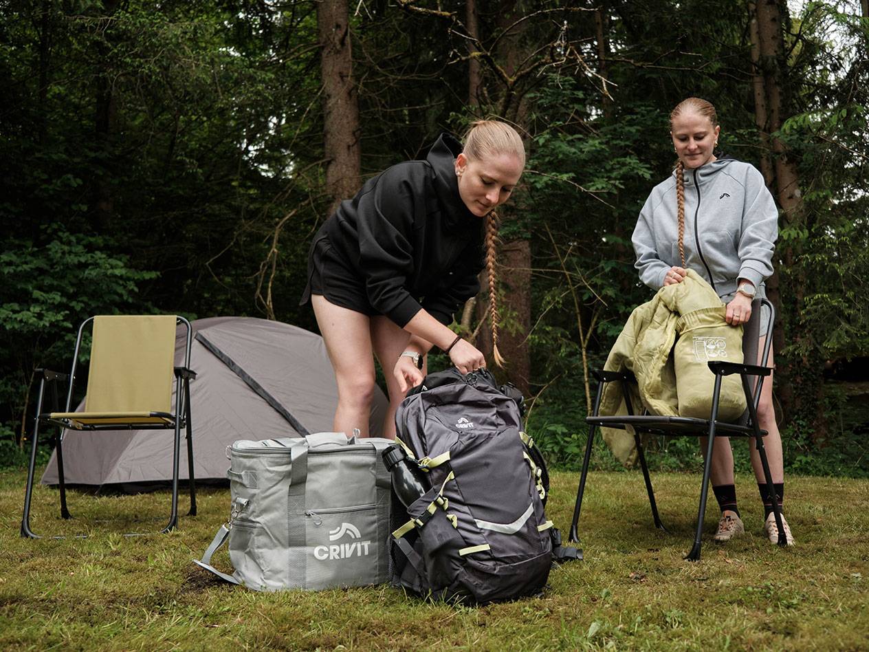 Zwei Frauen packen Campingausrüstung aus: Crivit Kühltasche und einen Rucksack im Wald.