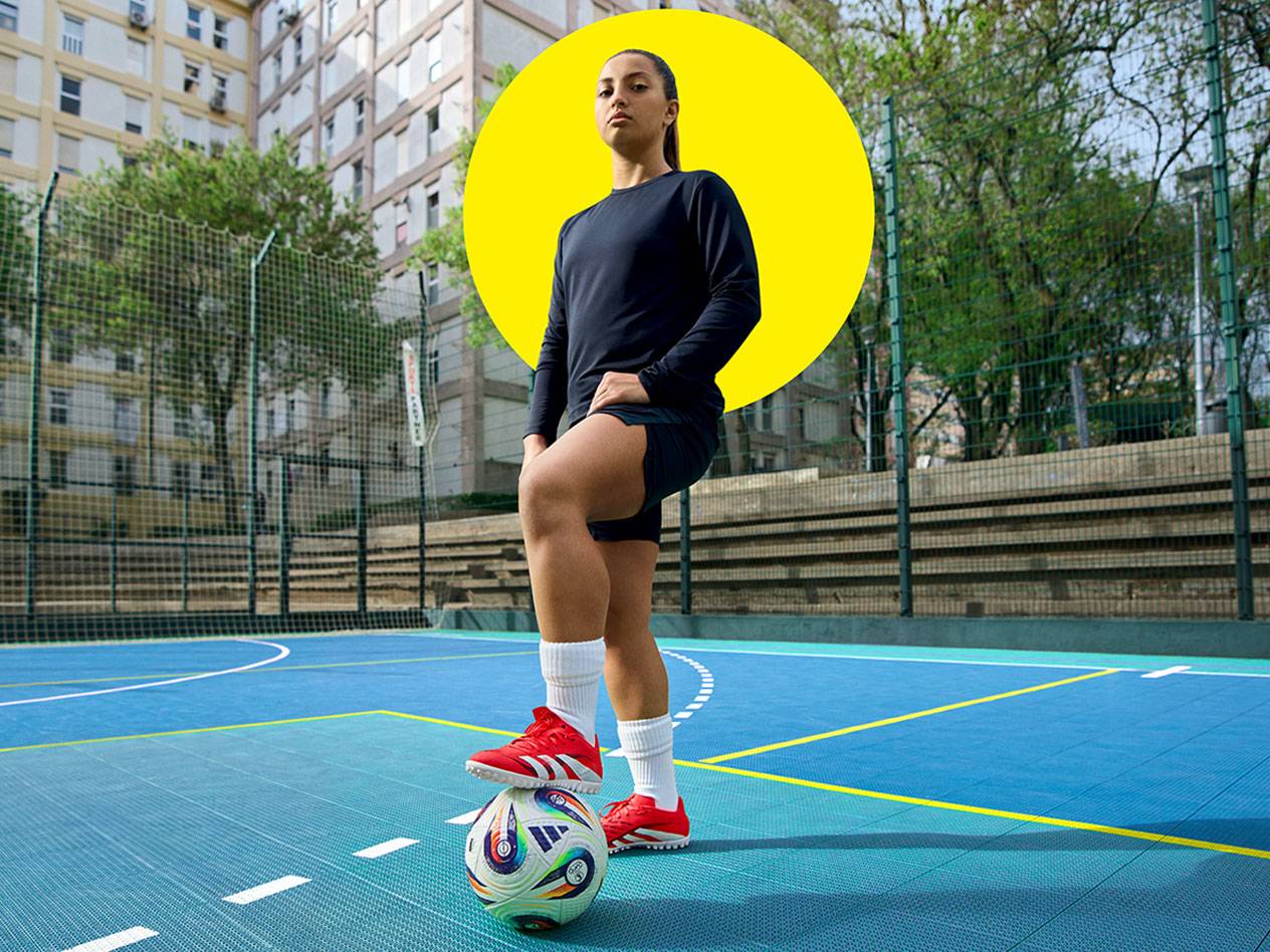 Fußballspielerin mit Adidas Schuhen auf einem blauen Platz.