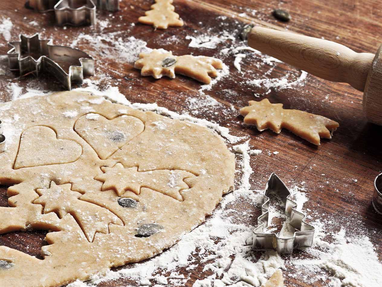 Plätzchenteig mit Ausstechformen und Ausstechplätzchen auf einem Holztisch.