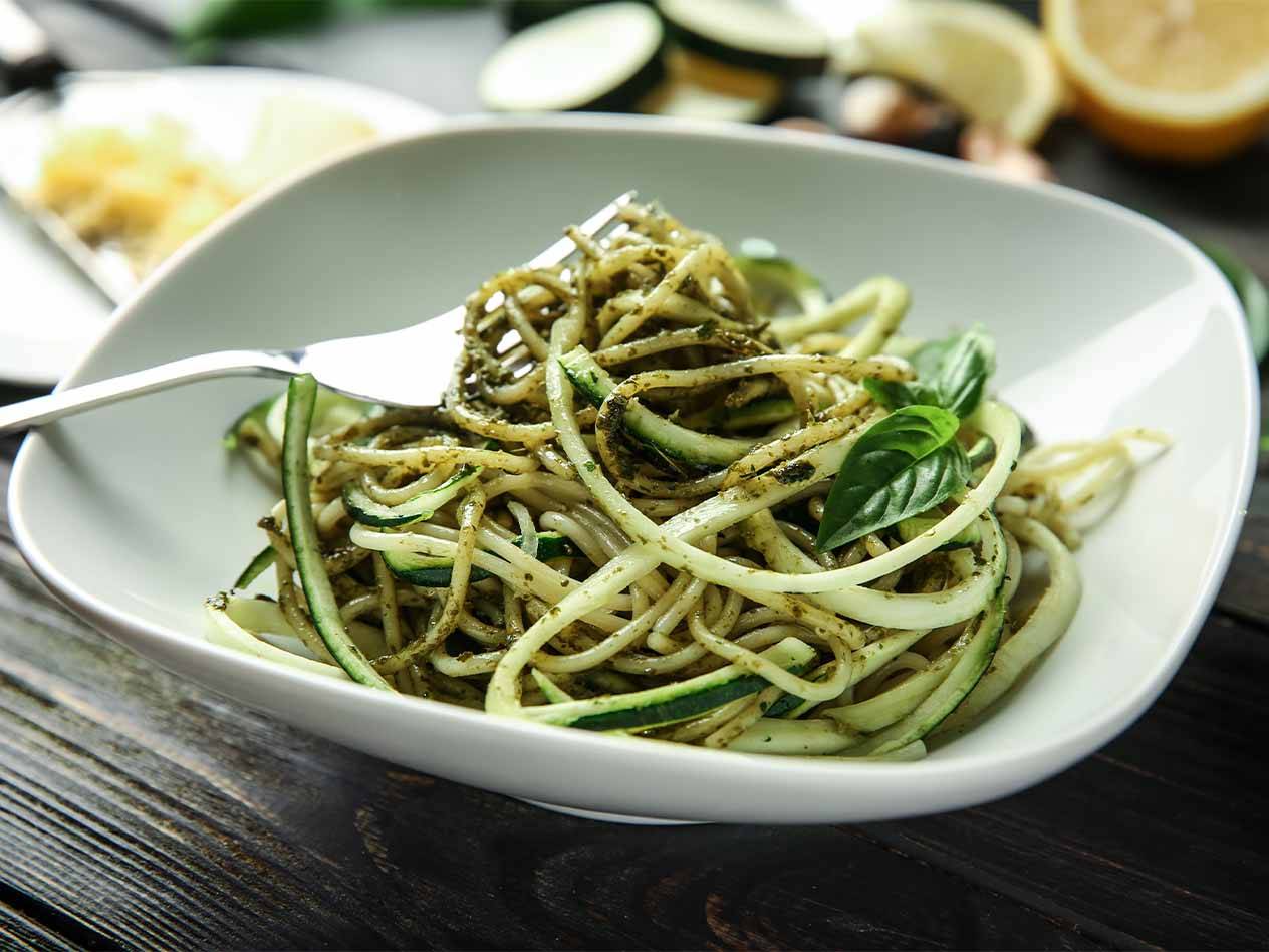 Zucchini-Nudeln mit Pesto und Basilikum in einer weißen Schale.