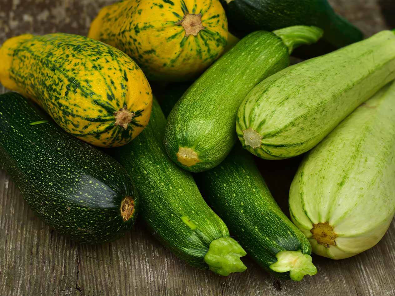 Eine Auswahl an Zucchini und Kürbissen in verschiedenen Grüntönen und Gelb auf Holz.
